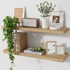 two wooden shelves with books, pictures and plants on them in front of a white wall