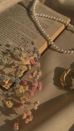 an open book with pearls and flowers on it next to a necklace that is laying on a table