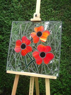 an easel with a stained glass painting on it and flowers in the center, sitting next to a green hedge