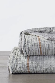 two folded towels sitting on top of each other in front of a white wall and wooden floor