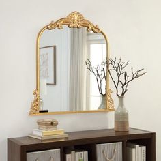 a mirror and some books on a shelf in front of a window with a vase