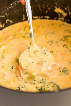 a ladle full of broccoli and cheese soup being stirred with a spoon