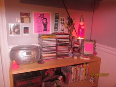 there is a book shelf with many books and cds on it in the corner next to a lamp