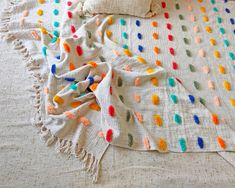 a blanket with multicolored dots on it laying on a bed next to two pillows