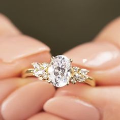 a woman's hand holding an oval diamond ring with three smaller diamonds on it