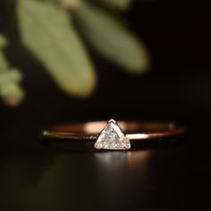 a gold ring with a pear shaped diamond in the center on a black surface next to a plant