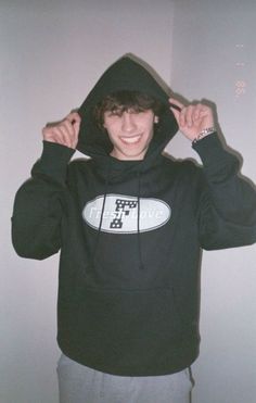 a young man in a black hoodie is holding his hands up to his ears