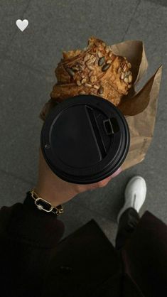 a person holding a coffee cup with food in it's hand and paper bag over their head