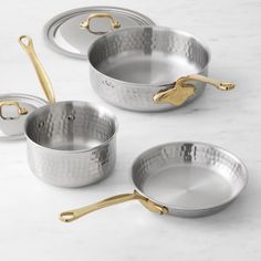 three stainless steel pots and pans with gold handles on a marble countertop top