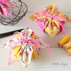 two small yellow and pink flowered bags next to some sewing needles on a white table