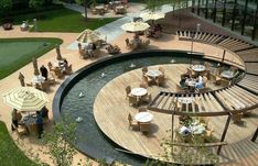 an aerial view of tables and umbrellas on a deck near a pond in the middle of a park