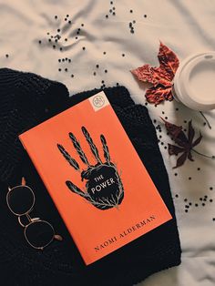 an orange book sitting on top of a bed next to a pair of glasses and a cup