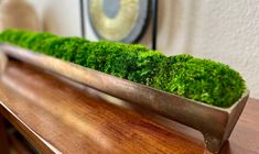 a wooden table topped with a metal vase filled with green moss