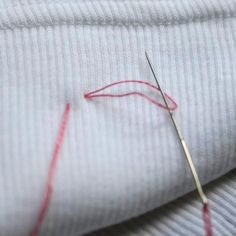 a pair of scissors and thread on top of a white t - shirt with red stitching