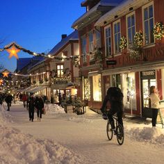 people are walking and riding bicycles in the snow on a city street at christmas time