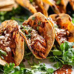 three tacos with meat, cheese and cilantro on a white tablecloth