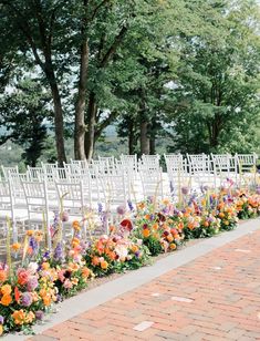 an outdoor ceremony with rows of white chairs and colorful flowers on the side walk way