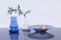 three glass vases are sitting on a table with one fruit in the bowl and another behind it