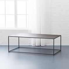 a black coffee table in front of a white brick wall and window with curtains behind it