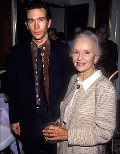 an older woman and young man standing next to each other in a room full of people