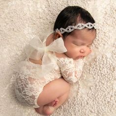 a newborn baby wearing a white lace outfit and headband laying on a blanket with her eyes closed