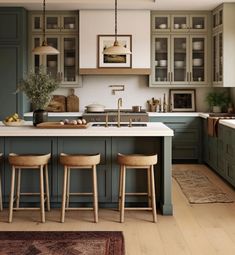 a kitchen with green cabinets and stools in the center, an island counter is flanked by three wooden bar stools