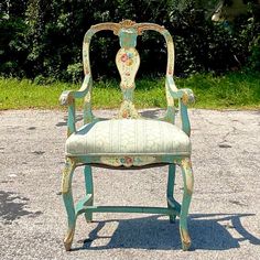 an old chair sitting in the middle of a parking lot with grass and bushes behind it