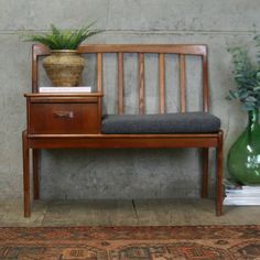 a wooden bench sitting next to a green vase with a plant on top of it