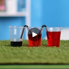 three shot glasses filled with red liquid sitting on top of a green grass covered field