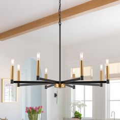 a chandelier hanging over a kitchen island with flowers on the table and windows in the background