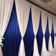 a blue and white wedding backdrop with flowers on the side, along with drapes