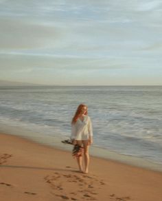 a woman is walking on the beach with flowers in her hand and footprints in the sand