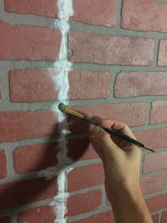 a person holding a paintbrush in front of a brick wall