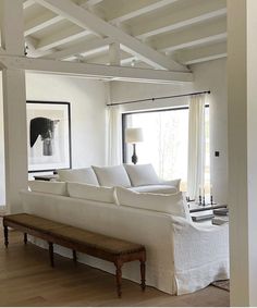 a large white couch sitting in a living room next to a wooden table and window