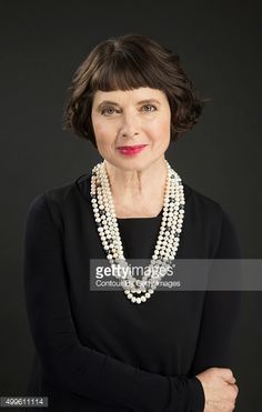 an older woman wearing pearls and a black dress with her arms crossed, looking at the camera