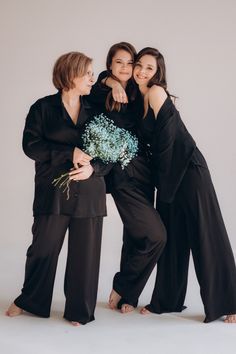 three women standing next to each other and hugging one another while holding a bouquet of flowers