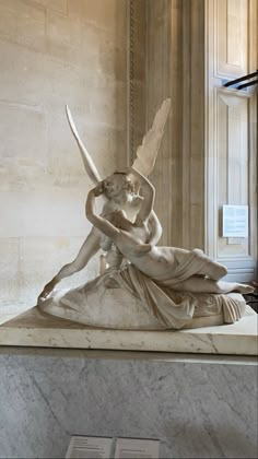 a statue of a woman sitting on top of a white marble slab in a building