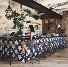 a woman sitting at a bar in front of an open air bar with stools