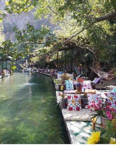 an outdoor seating area next to a river filled with flowers and greenery on both sides