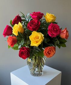 a vase filled with multi colored roses on top of a white table next to a gray wall