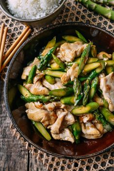 chicken and asparagus stir - fry in a brown bowl with chopsticks