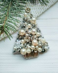 a small christmas tree made out of pearls and other beads on a white table next to a pine branch