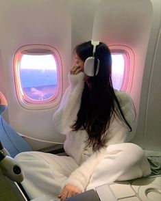 a woman sitting on an airplane seat with headphones in her ears looking out the window