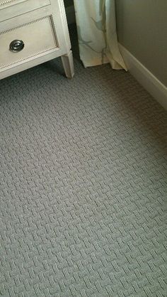 a white dresser sitting next to a bed in a bedroom on top of a carpeted floor