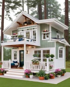 a white house with lots of windows and plants on the front porch, surrounded by tall pine trees