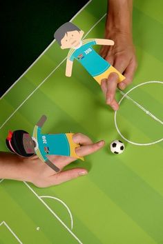 two hands reaching for a soccer ball on a green field with people's fingers