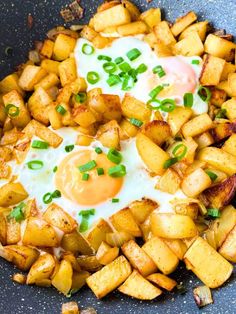 fried eggs and potatoes in a skillet with green onions