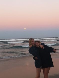 two women hugging each other on the beach at sunset with waves coming in and setting sun behind them