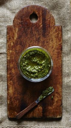 a wooden cutting board topped with a small bowl of pesto