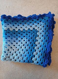 a blue and white crocheted pillow sitting on the floor next to a carpet